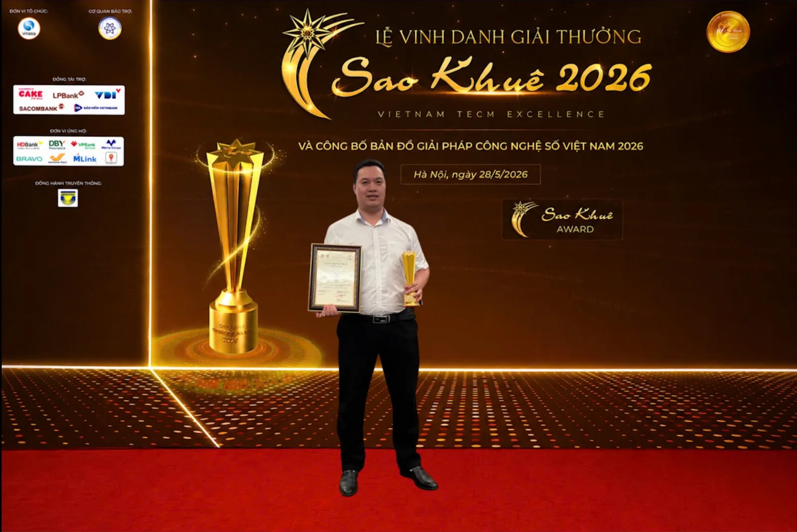 Người nhận giải cầm giấy chứng nhận và cúp trước phông nền lễ vinh danh Sao Khuê 2026